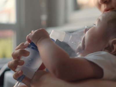 Child lying on bed with nebuliser mask on face.